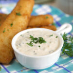Fish sticks are placed by a small white cup of tartar sauce.