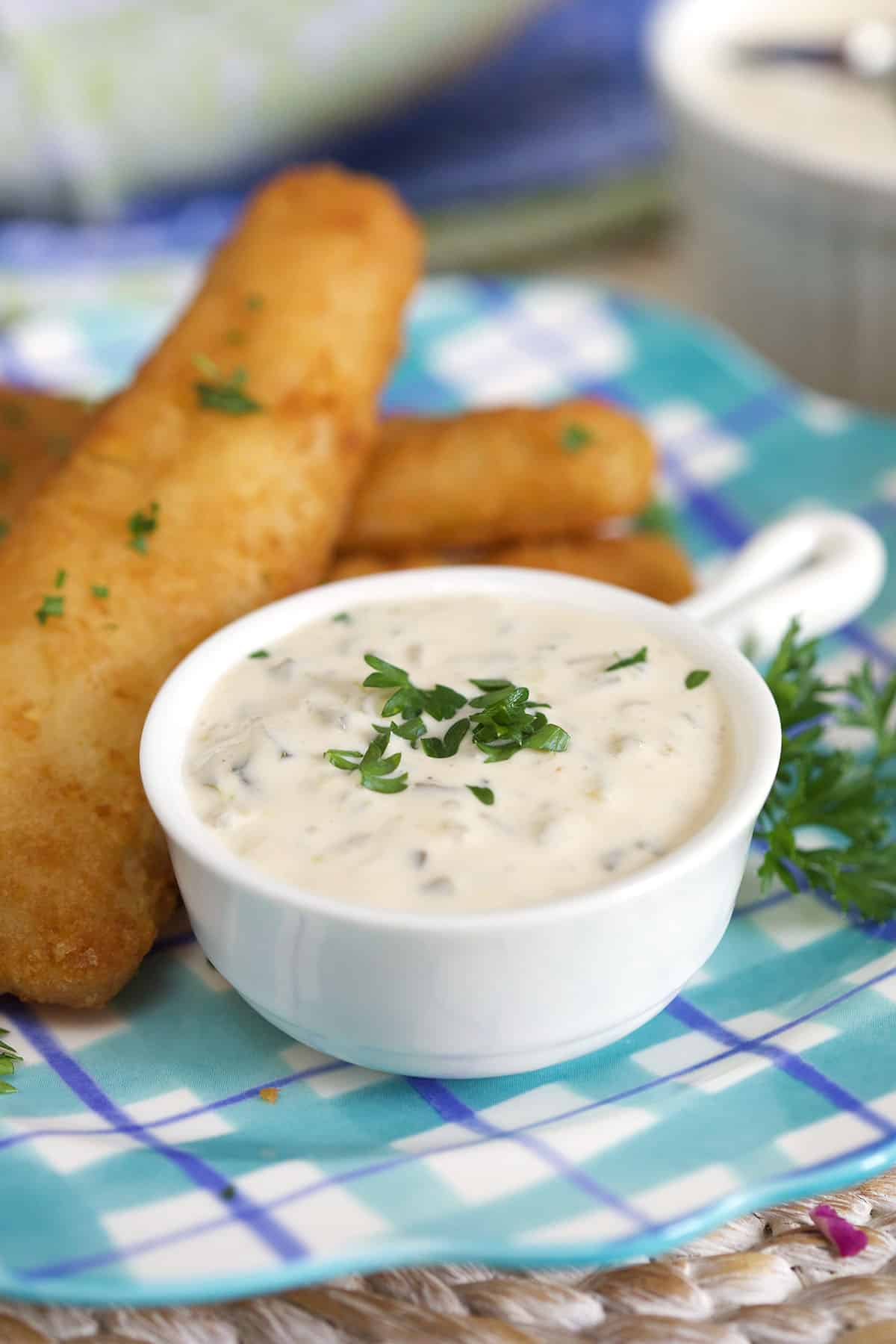 Fish sticks are placed by a small white cup of tartar sauce. 
