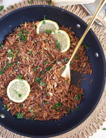 Cooked orzo is topped with fresh parsley in a skillet.