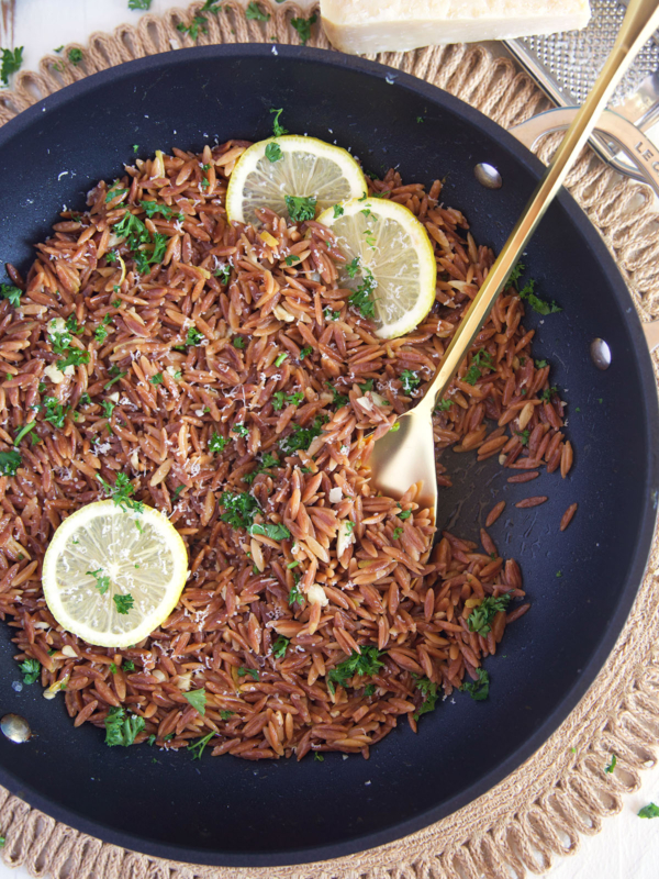 Cooked orzo is topped with fresh parsley in a skillet.