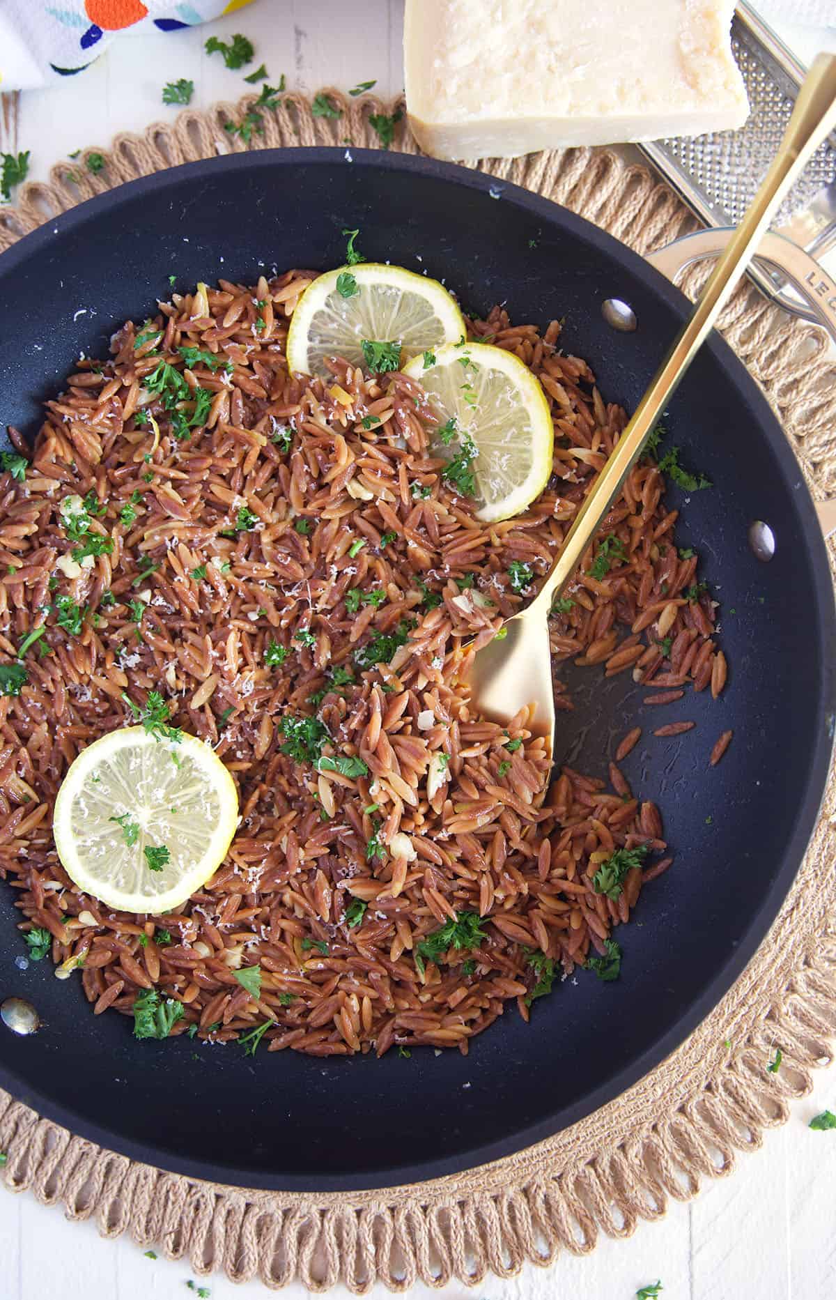 Cooked orzo is topped with fresh parsley in a skillet. 