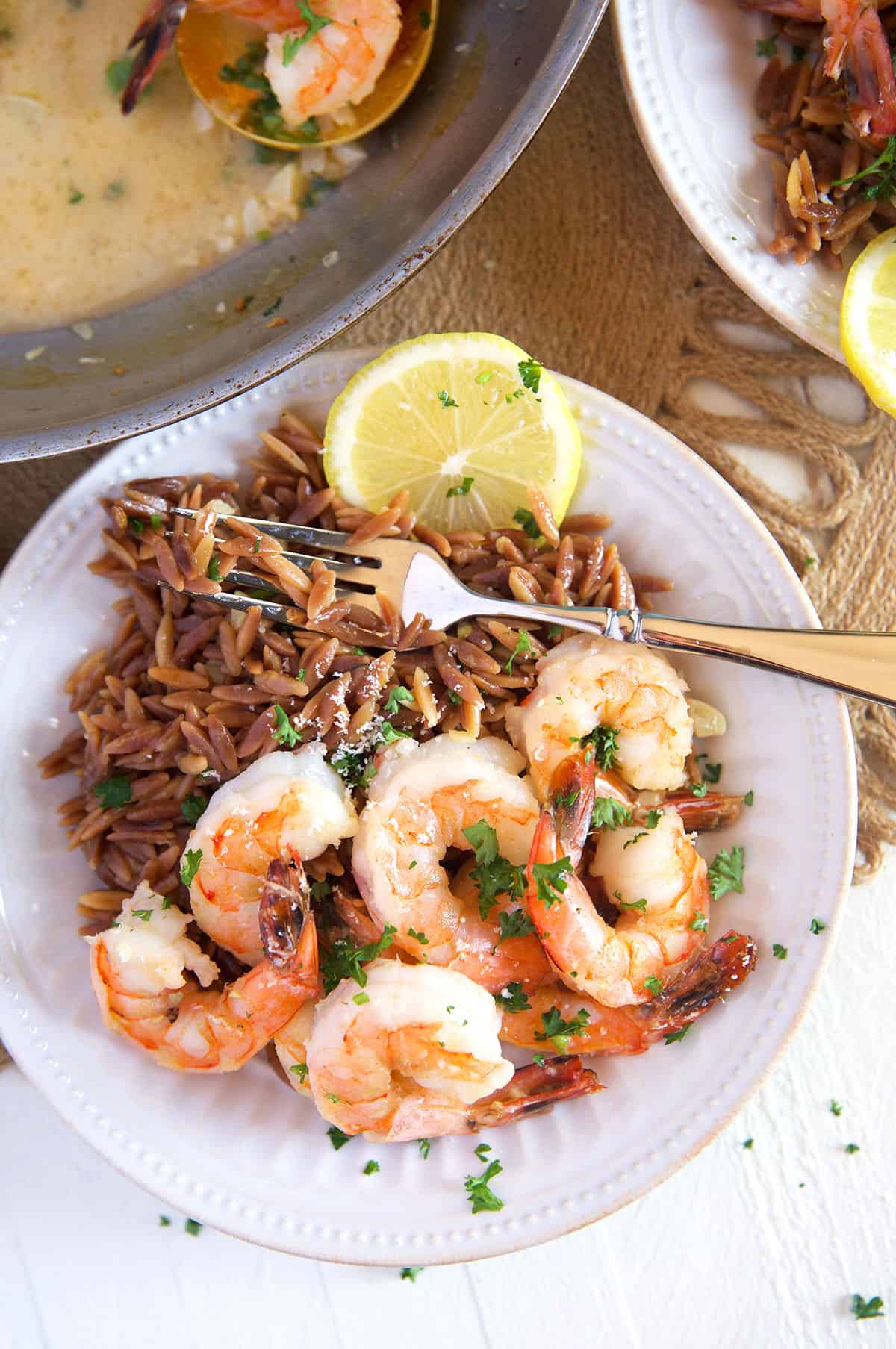 Orzo and shrimp are both placed in a white bowl with a lemon wedge. 