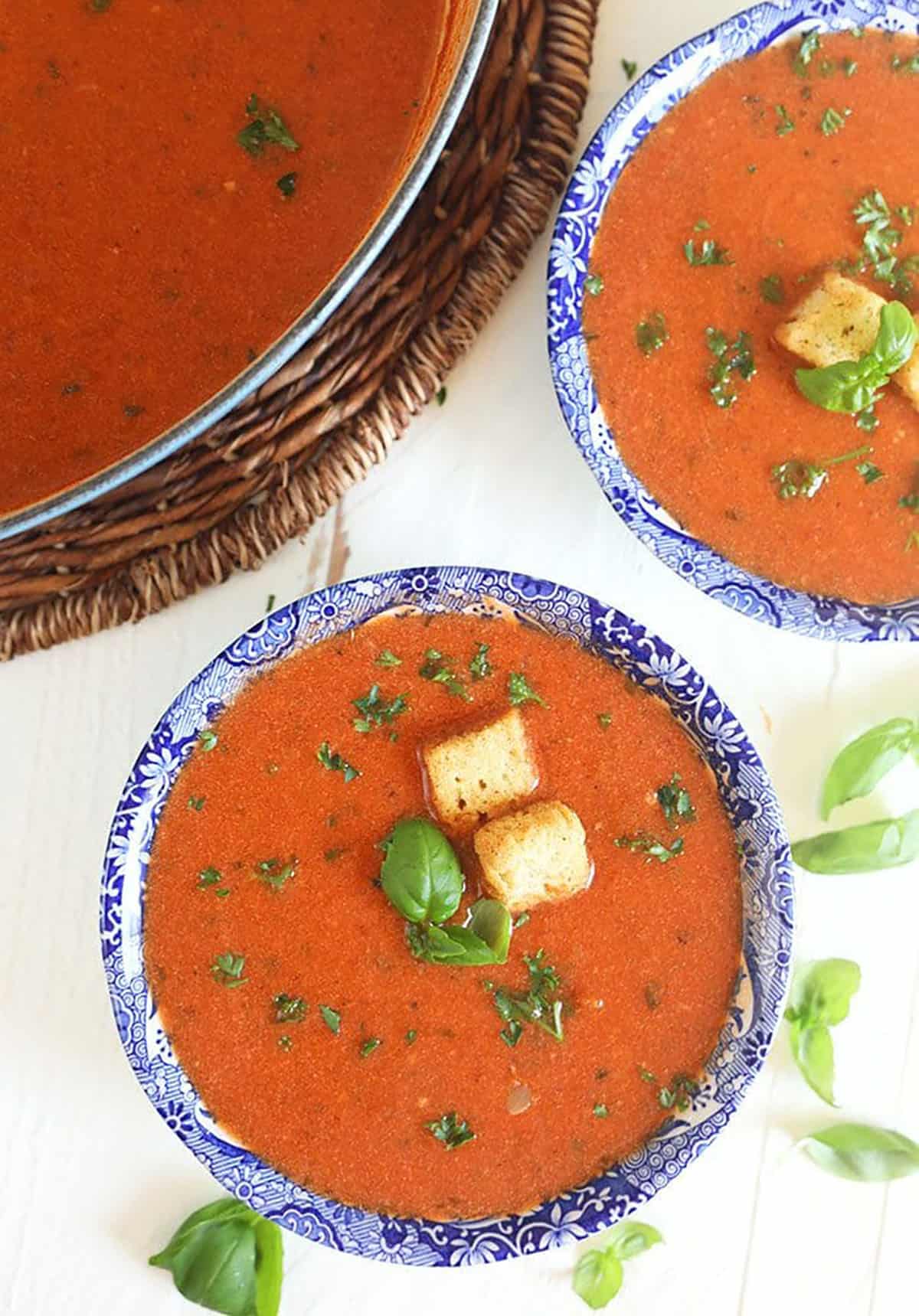 Overhead shot of tomato basil bisque with croutons in a blue and white bowl on a white background.