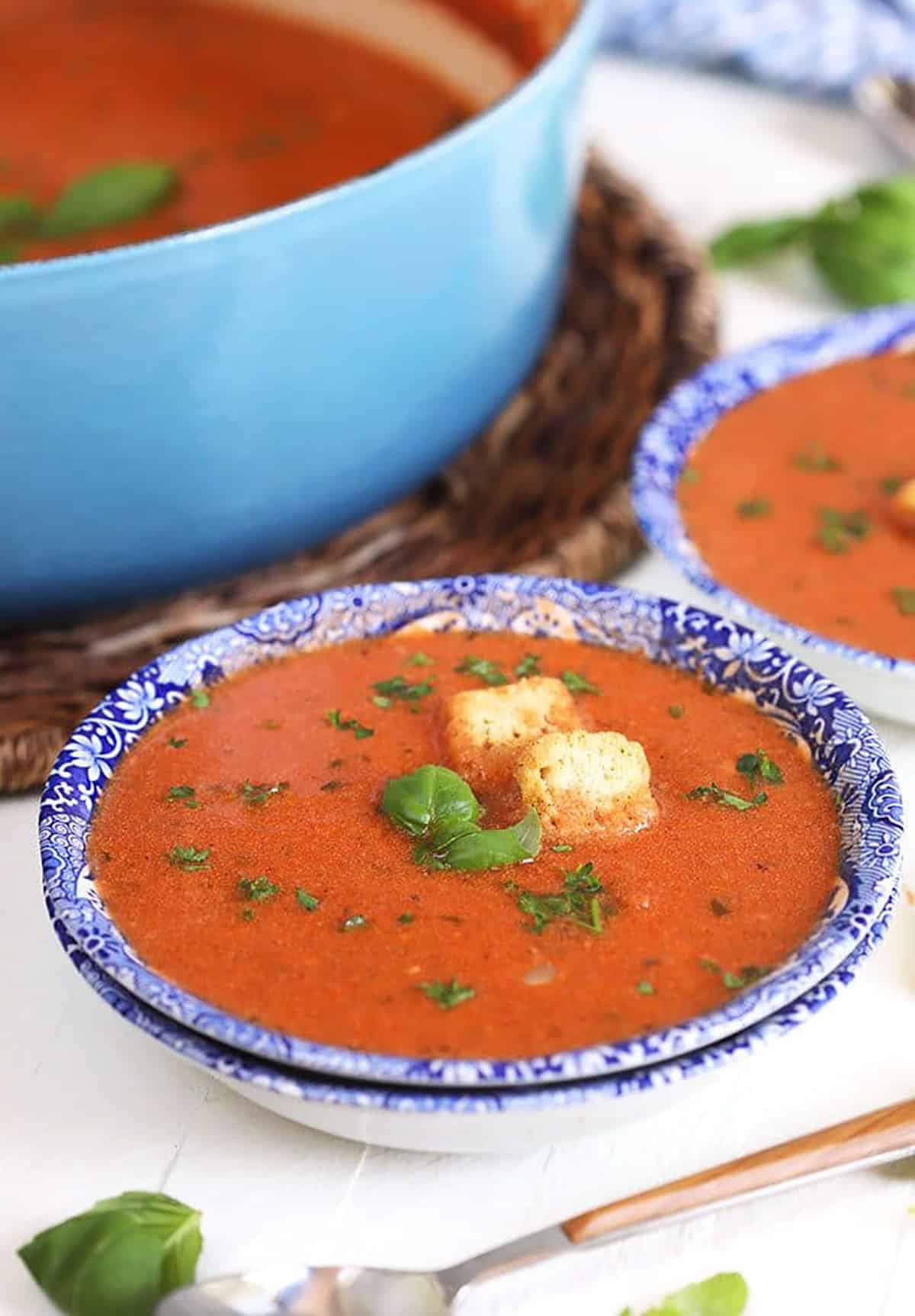 Tomato Basil Bisque in a blue and white bowl with croutons and basil on a white background.