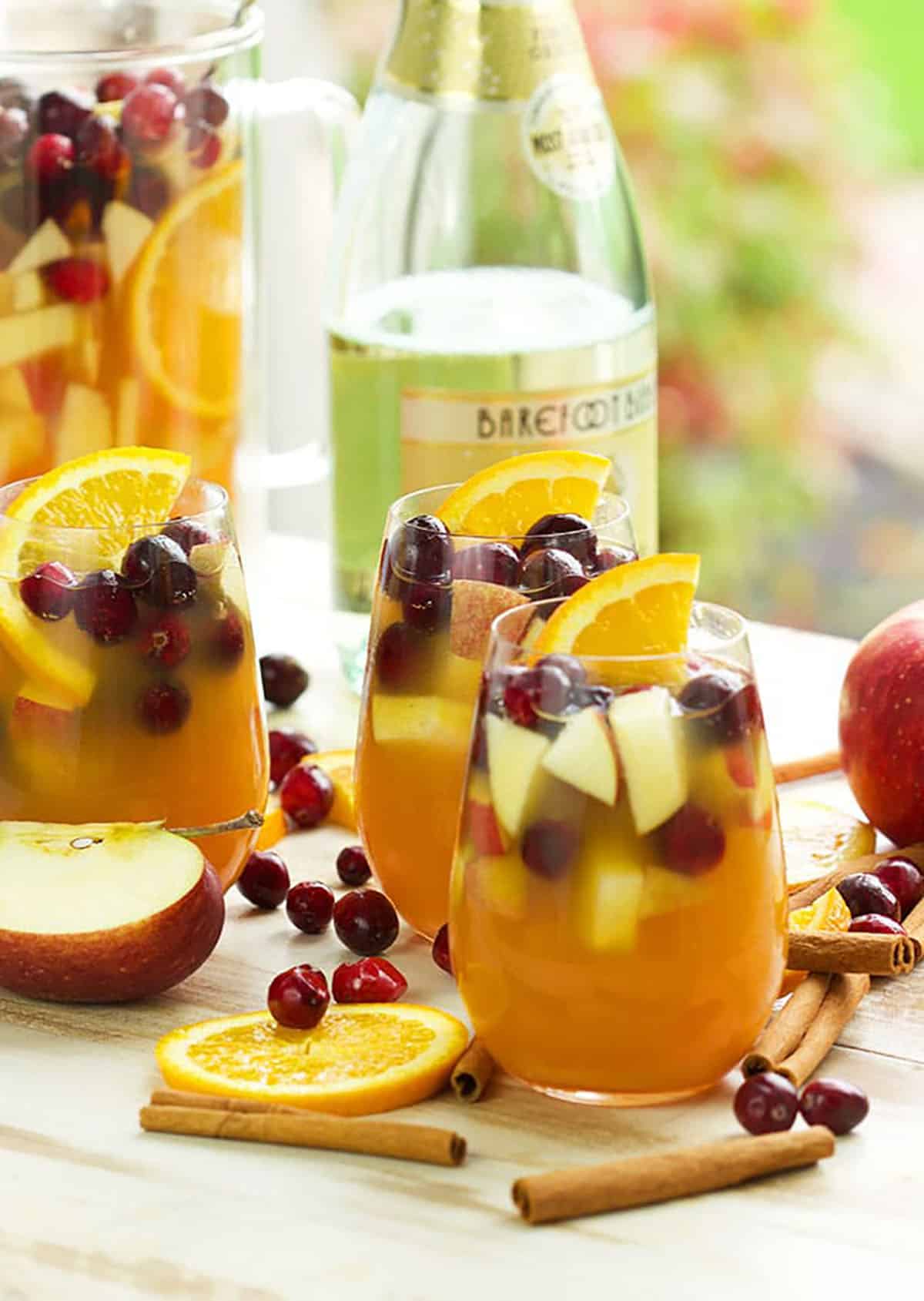 Three glasses filled with apple cider sangria, cranberries, orange slices and apples.