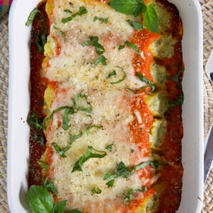 A white baking dish is filled with baked stuffed manicotti.
