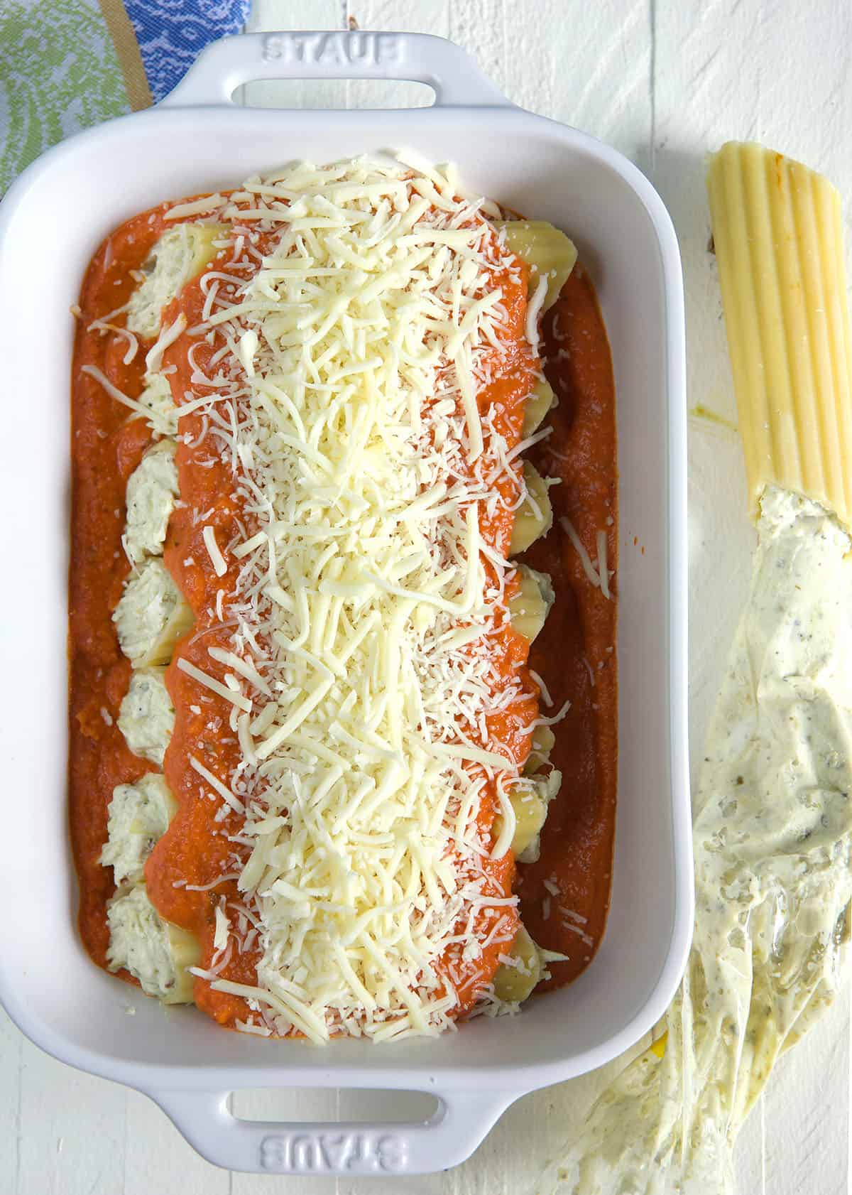 Stuffed manicotti is covered in uncooked cheese and sauce. 