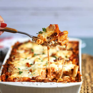 The Very Best Baked Ziti recipe in a white baking dish with a spoonful being scooped out and stretchy melty cheese
