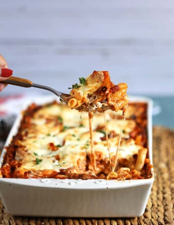 The Very Best Baked Ziti recipe in a white baking dish with a spoonful being scooped out and stretchy melty cheese