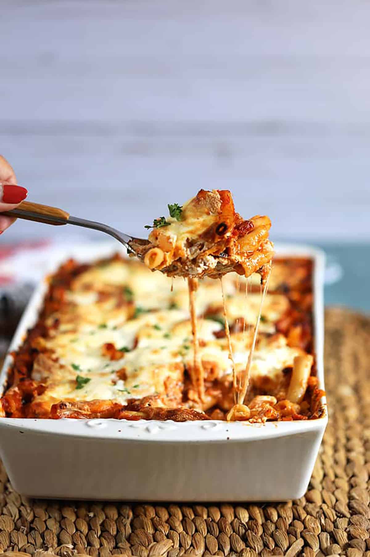 The Very Best Baked Ziti recipe in a white baking dish with a spoonful being scooped out and stretchy melty cheese