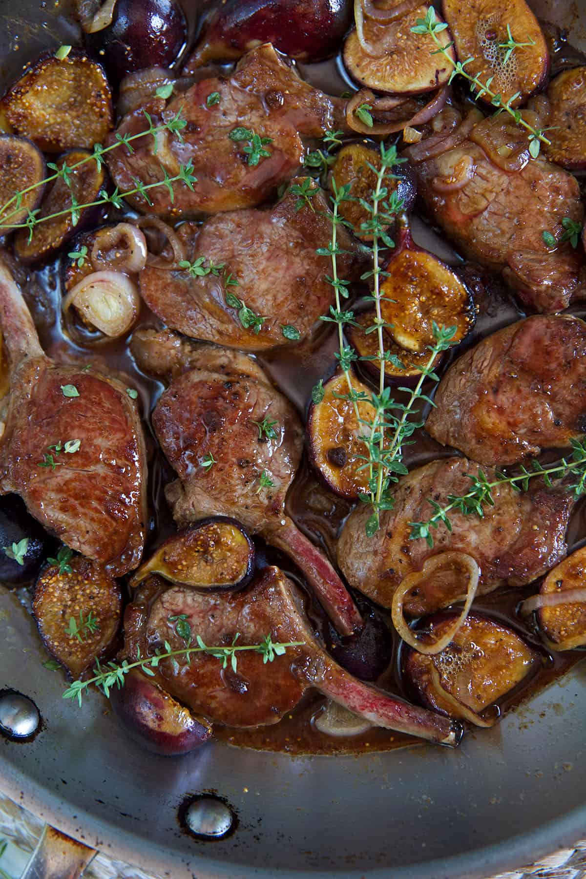 Fully cooked meat, figs, and fresh herbs are in a saucy pan.