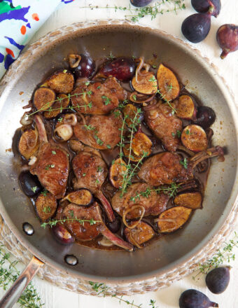 Lamb, figs, and herbs are cooking in a large metal pan.