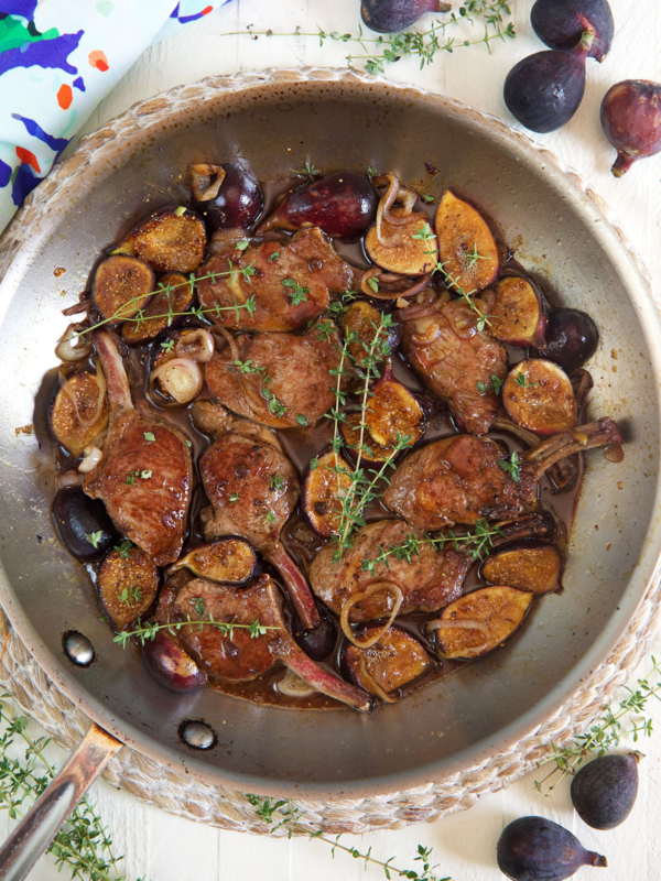 Lamb, figs, and herbs are cooking in a large metal pan.