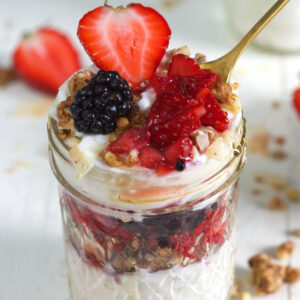 A small glass jar is filled to the brim with granola, berries, and yogurt.