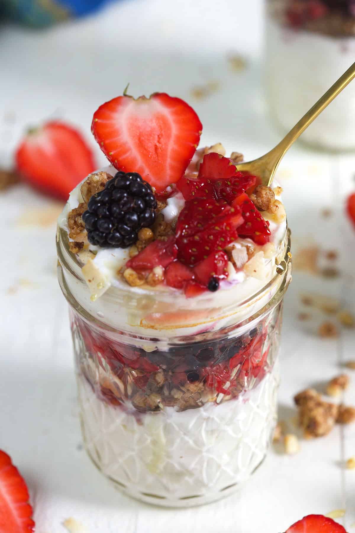 A small glass jar is filled to the brim with granola, berries, and yogurt. 