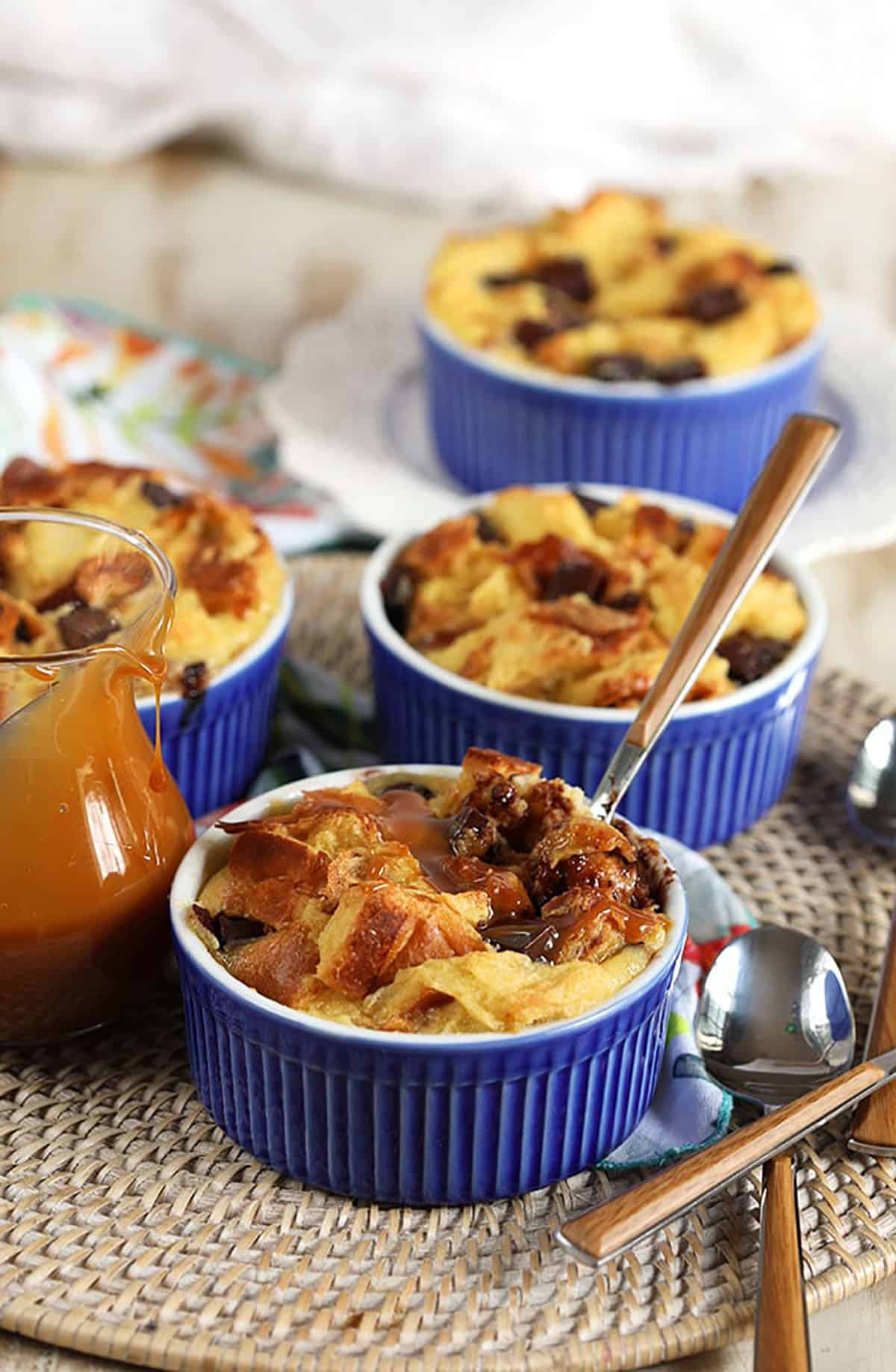 Three blue ramekins with bread pudding in them and a wood spoon sticking out of the front bread pudding dish.