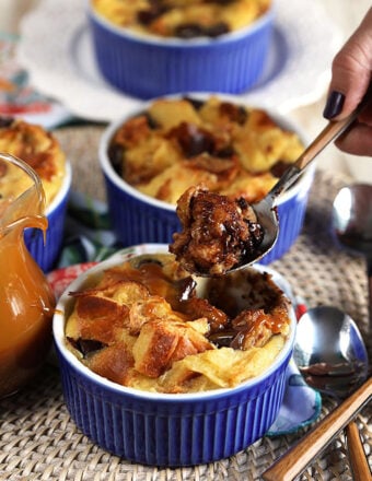 Brioche bread pudding in a blue ramekin with a wooden spoon digging into it.