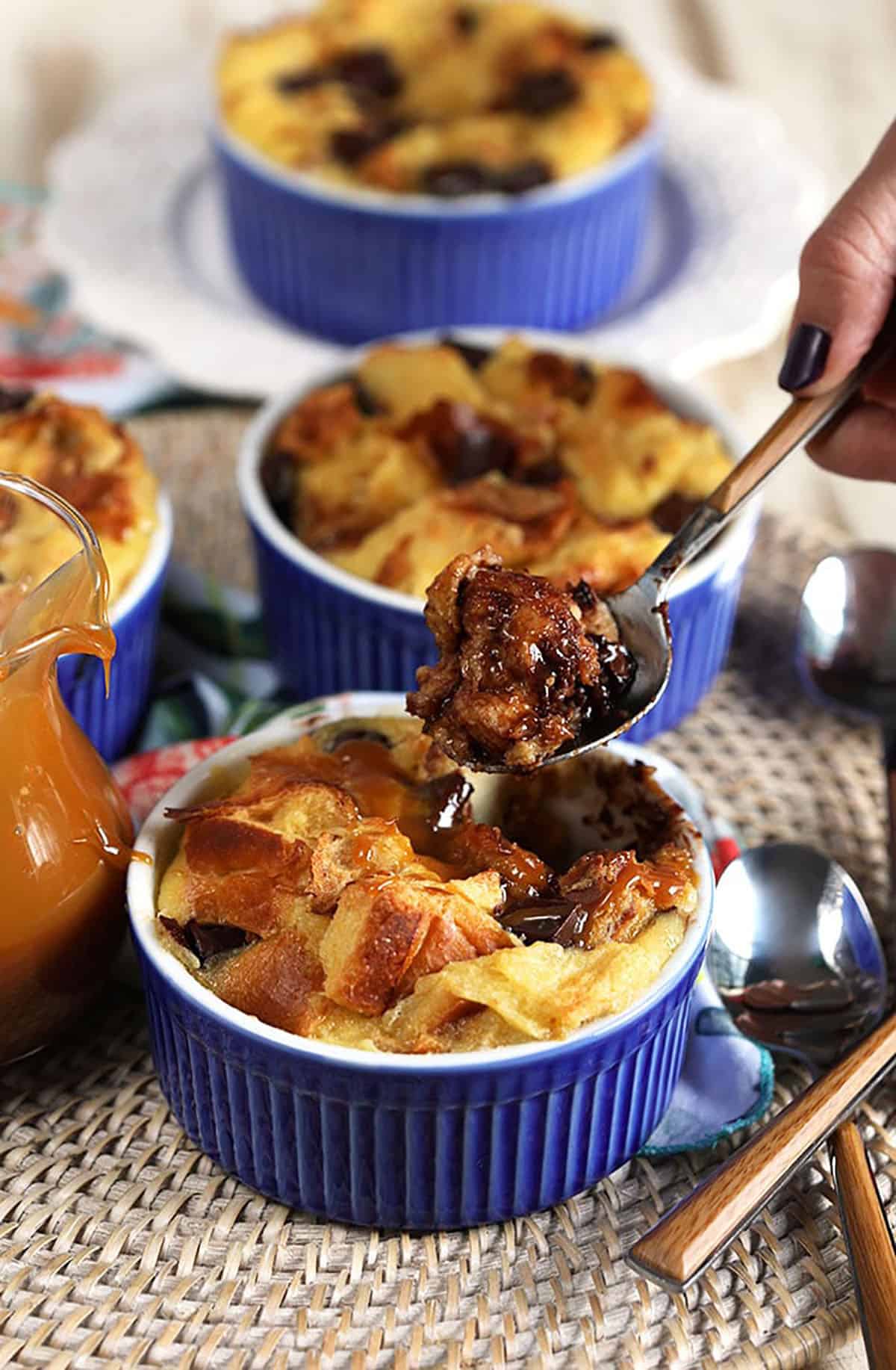Brioche bread pudding in a blue ramekin with a wooden spoon digging into it.