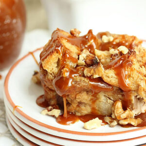 caramel apple bread pudding on a white plate with a jar of caramel sauce in the background.