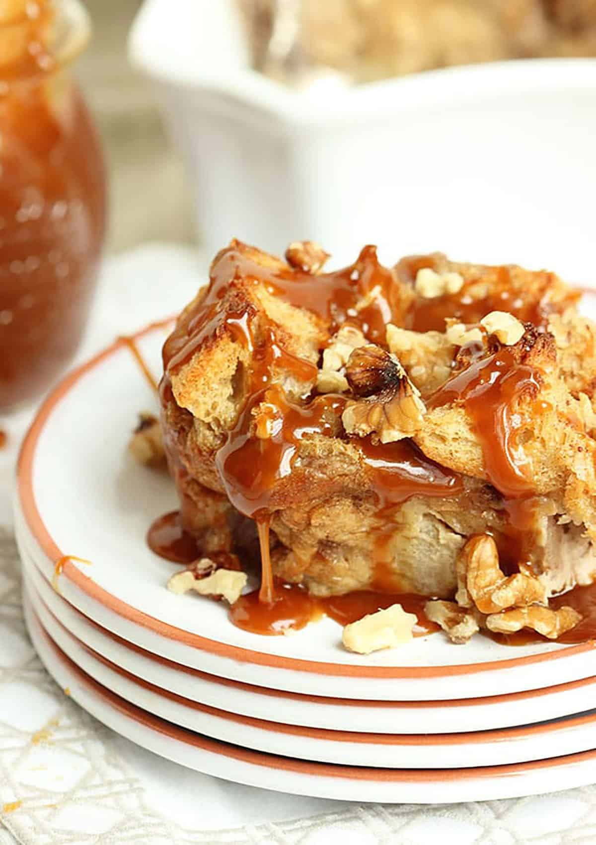 caramel apple bread pudding on a white plate with a jar of caramel sauce in the background.