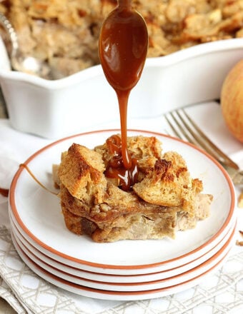 a slice of caramel apple bread pudding being drizzled with caramel sauce with a spoon.