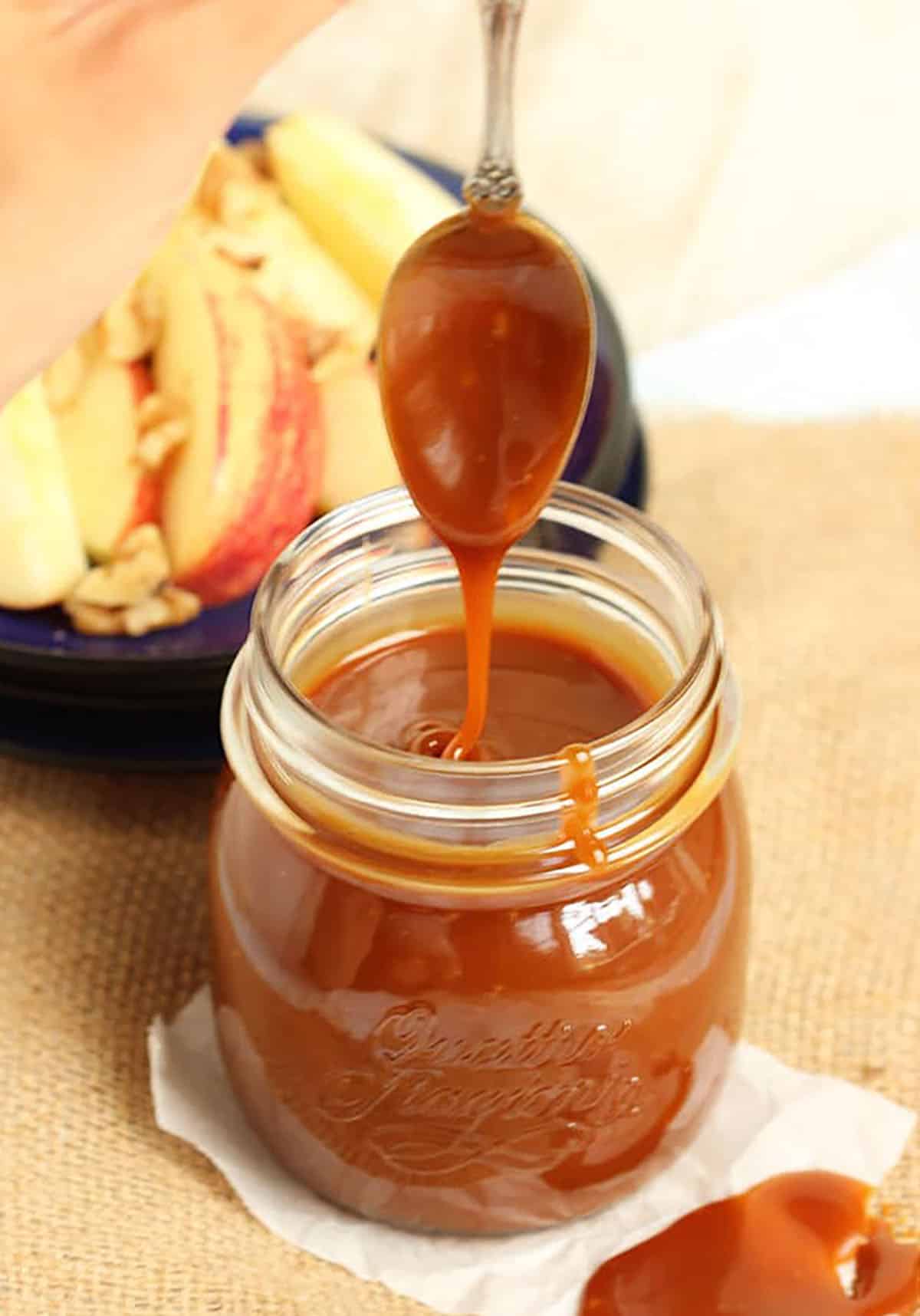 A jar of caramel sauce with a spoon drizzling it back into the jar.