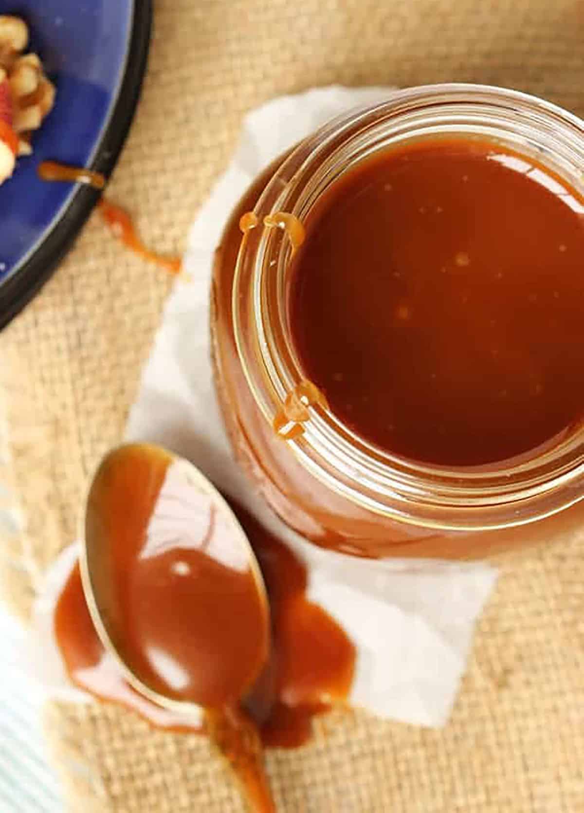 Caramel Sauce in a canning jar with a spoon filled with caramel sauce set next to it.