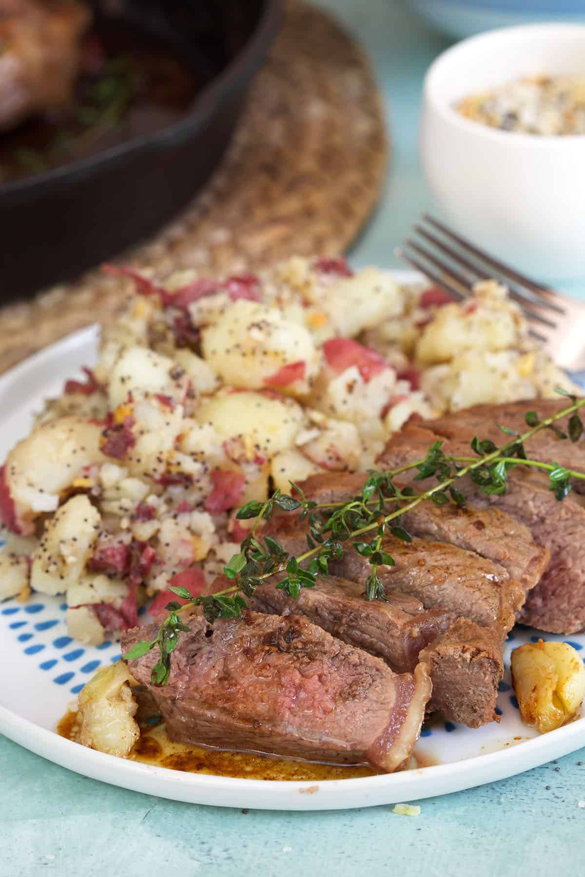 Steak and potatoes are served with fresh thyme on a blue and white plate.