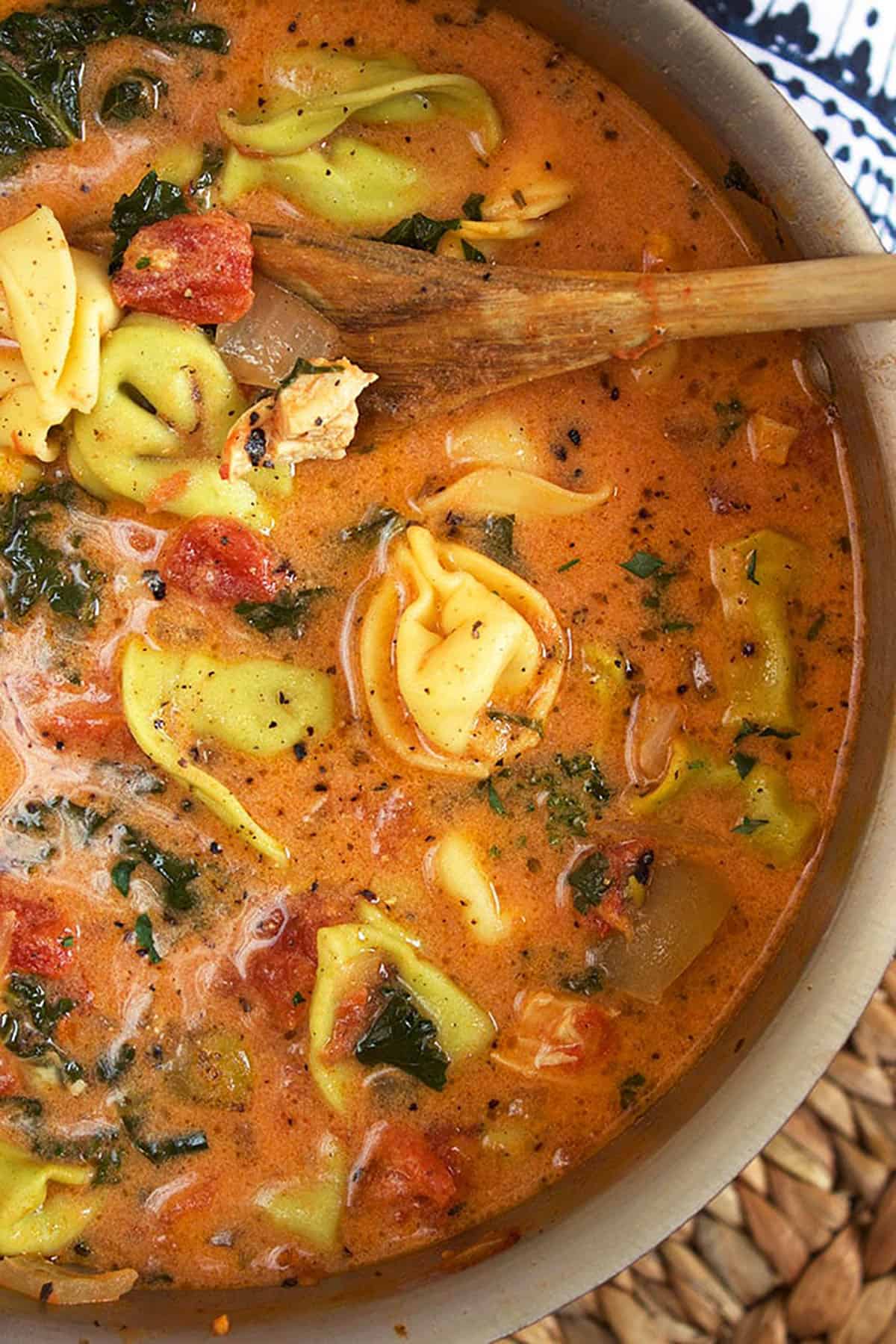 creamy chicken tortellini soup in a pot with a wooden spoon in it.