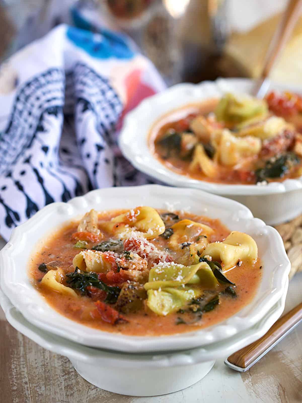 two bowls stacked with chicken tortellini soup in them and a floral napkin behind it