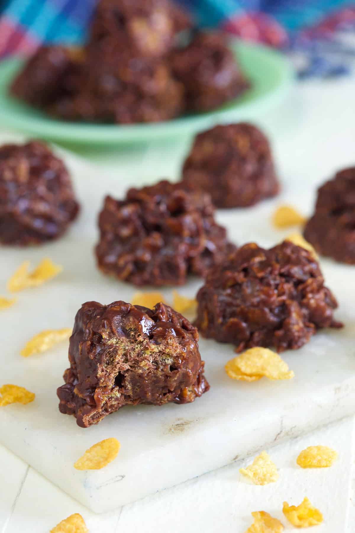 Several pieces of chocolate cornflake candy are placed next to cereal bits on a white surface. 