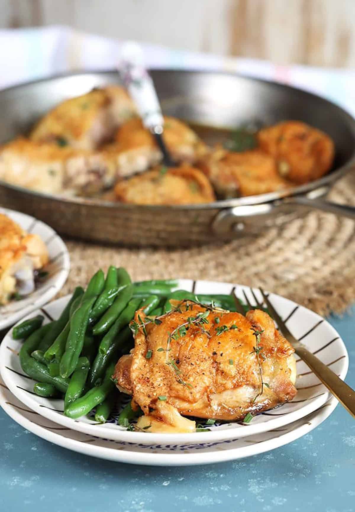 Close up of Crispy Baked Chicken Thighs on a white plate with green beans on a blue background.