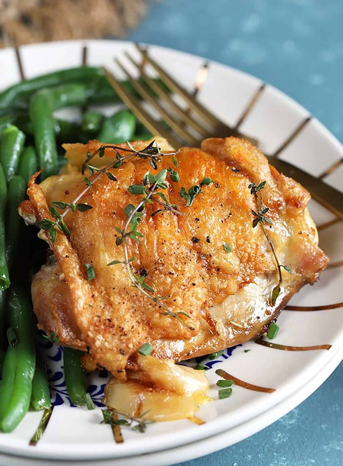 Crispy Baked Chicken Thighs with Garlic Herb Sauce on a white plate with green beans.