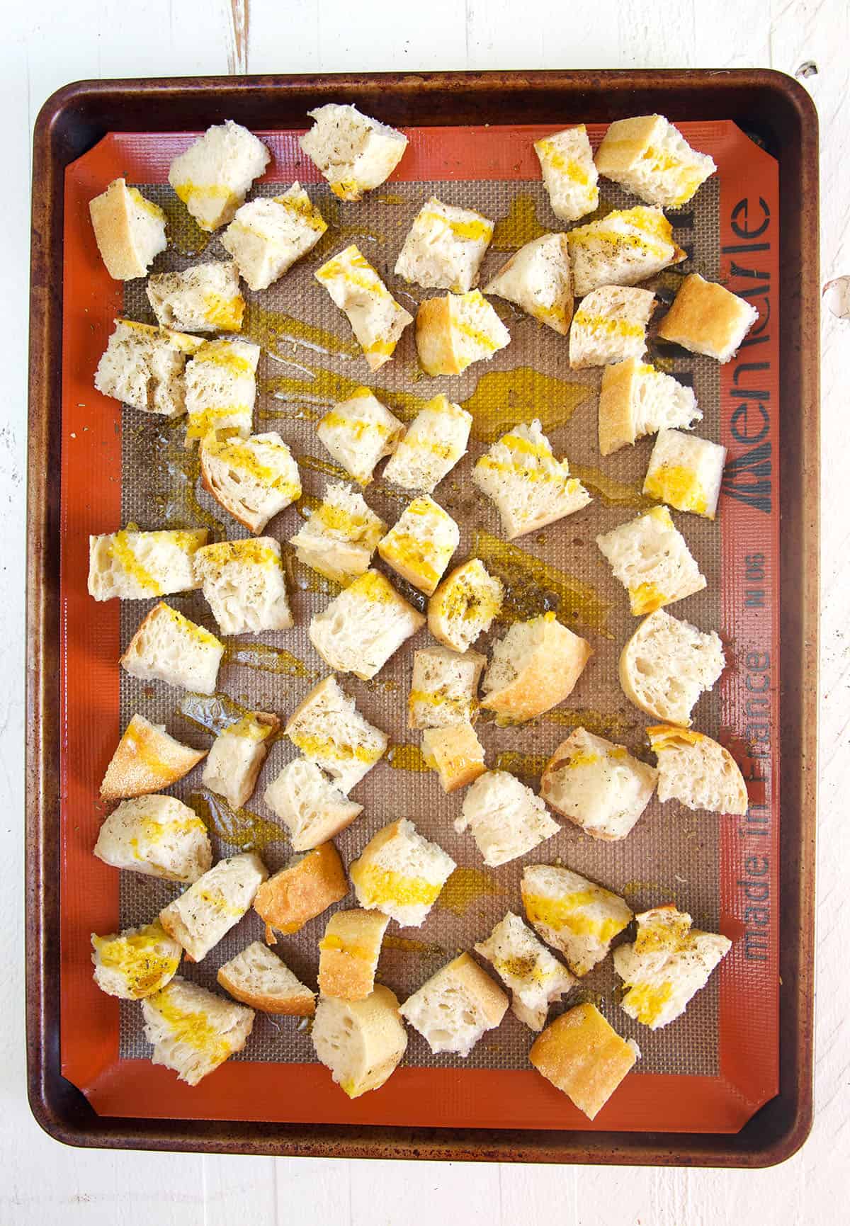 Croutons are drizzled with olive oil on a baking sheet and not yet cooked. 