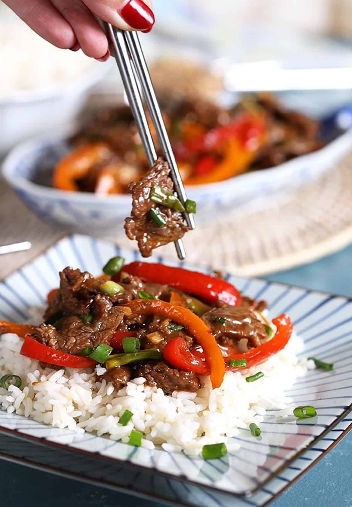 Mongolian Beef on a bed of white rice with a bite in silver chopsticks.