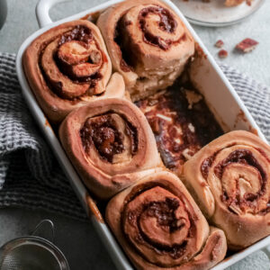 A cinnamon roll is missing from the white baking dish.