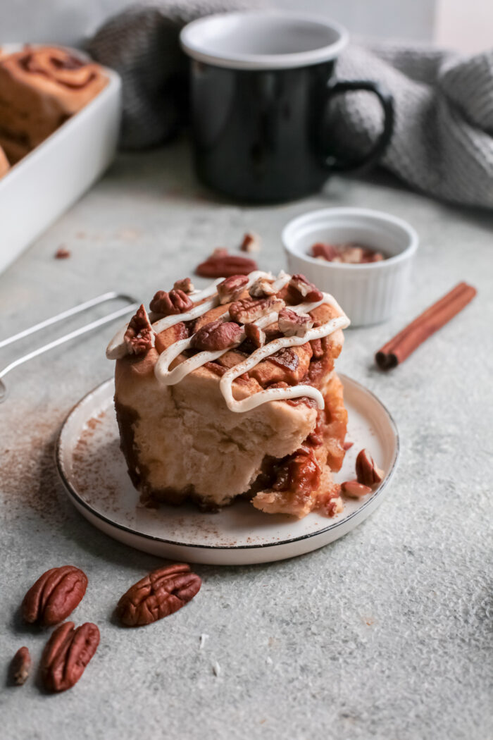 A single caramel pecan cinnamon roll is placed on a small white plate.
