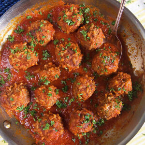 Overhead shot of porcupine meatballs in tomato sauce in a skillet with a spoon.