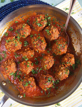 Overhead shot of porcupine meatballs in tomato sauce in a skillet with a spoon.