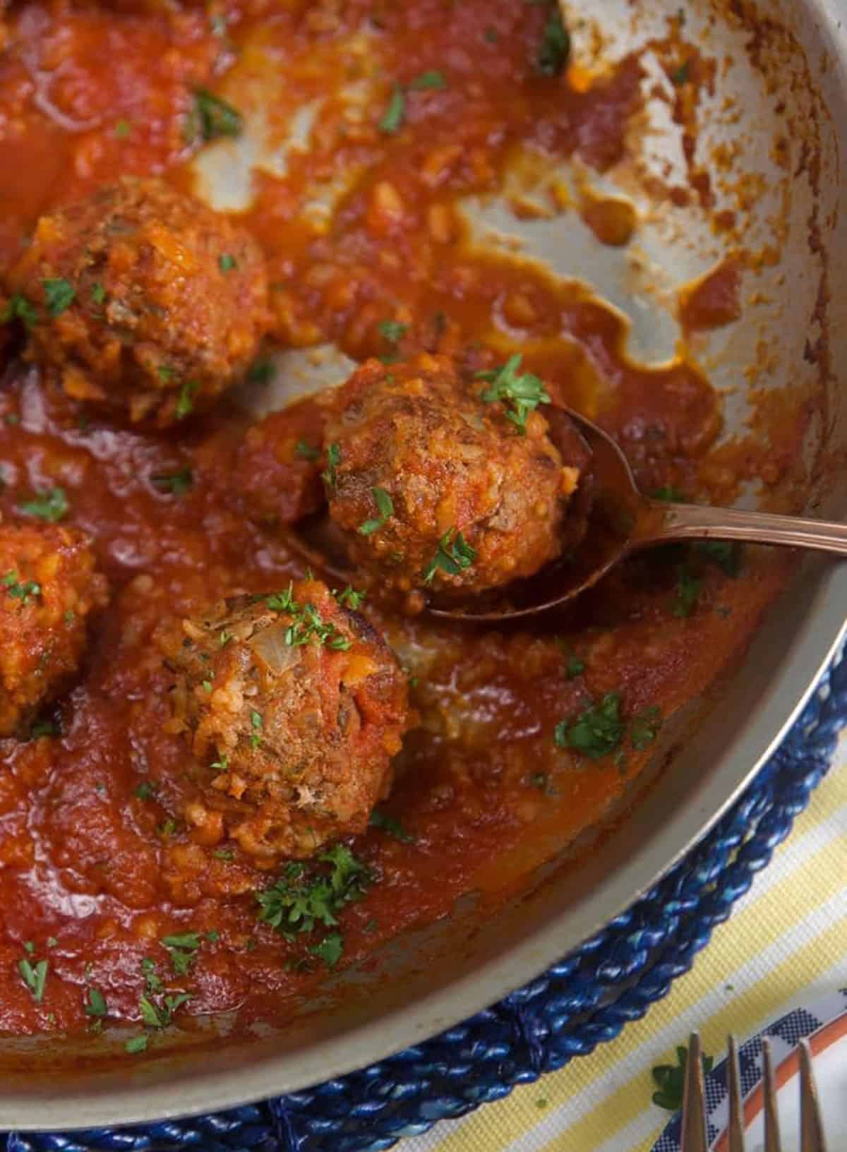 Porcupine meatballs in a skillet with a silver serving spoon.