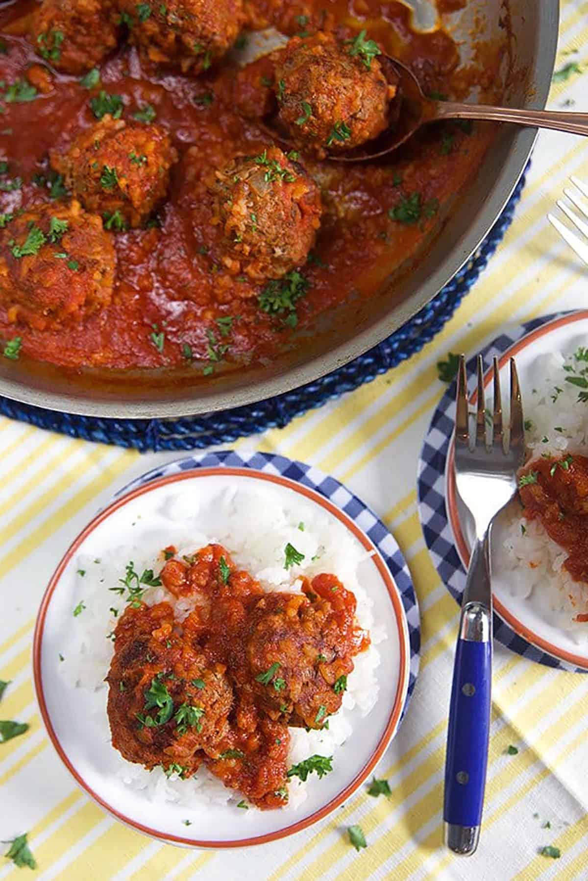 overhead shot of meatballs in a skillet with more meatballs on a white plate with a blue fork.