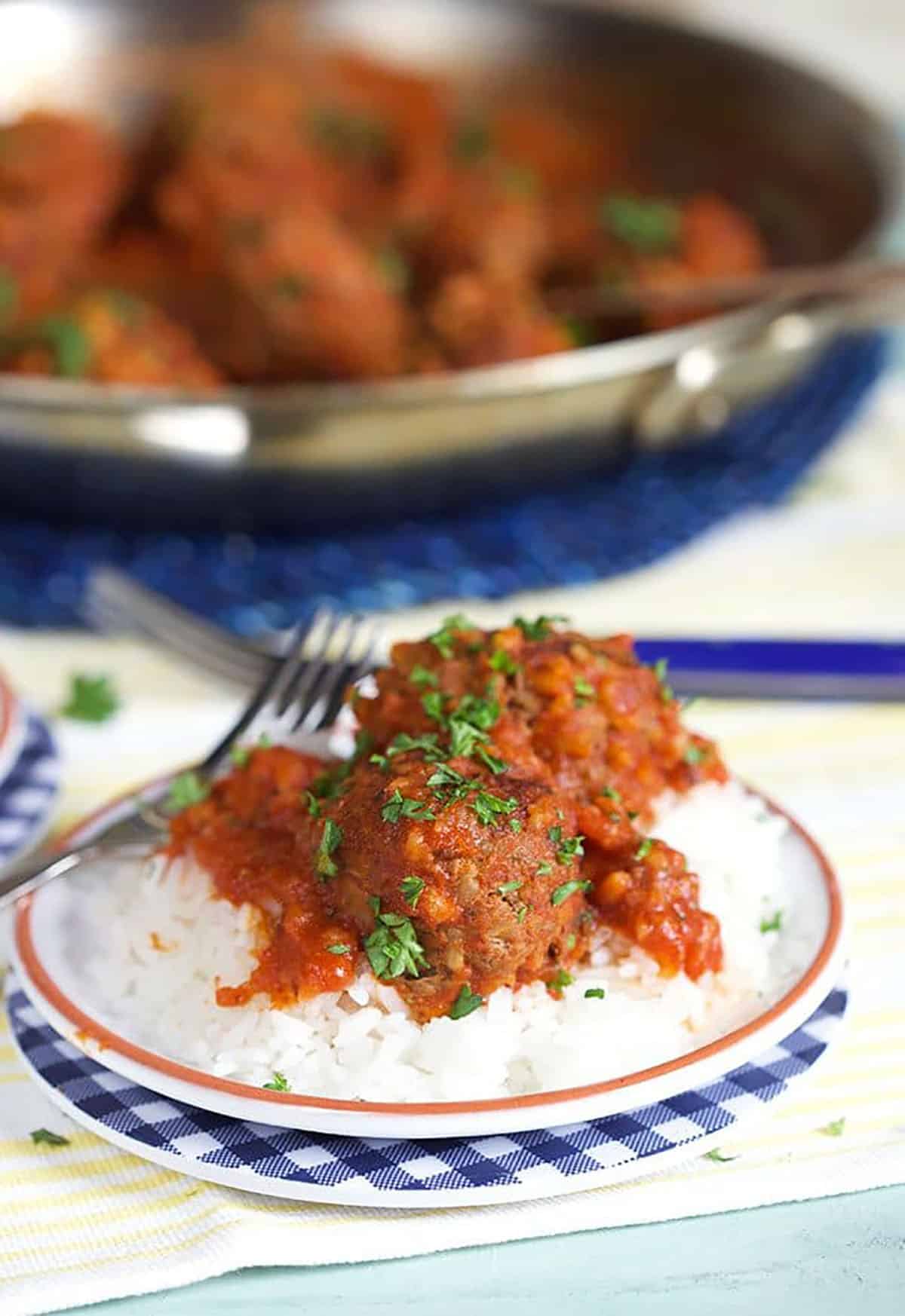 Easy Porcupine Meatballs in red sauce over a bed of rice with a skillet in the background.