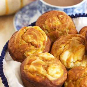 Pumpkin Cream Cheese Swirl Muffins in a basket with a white napkin and a cup of coffee in the background.