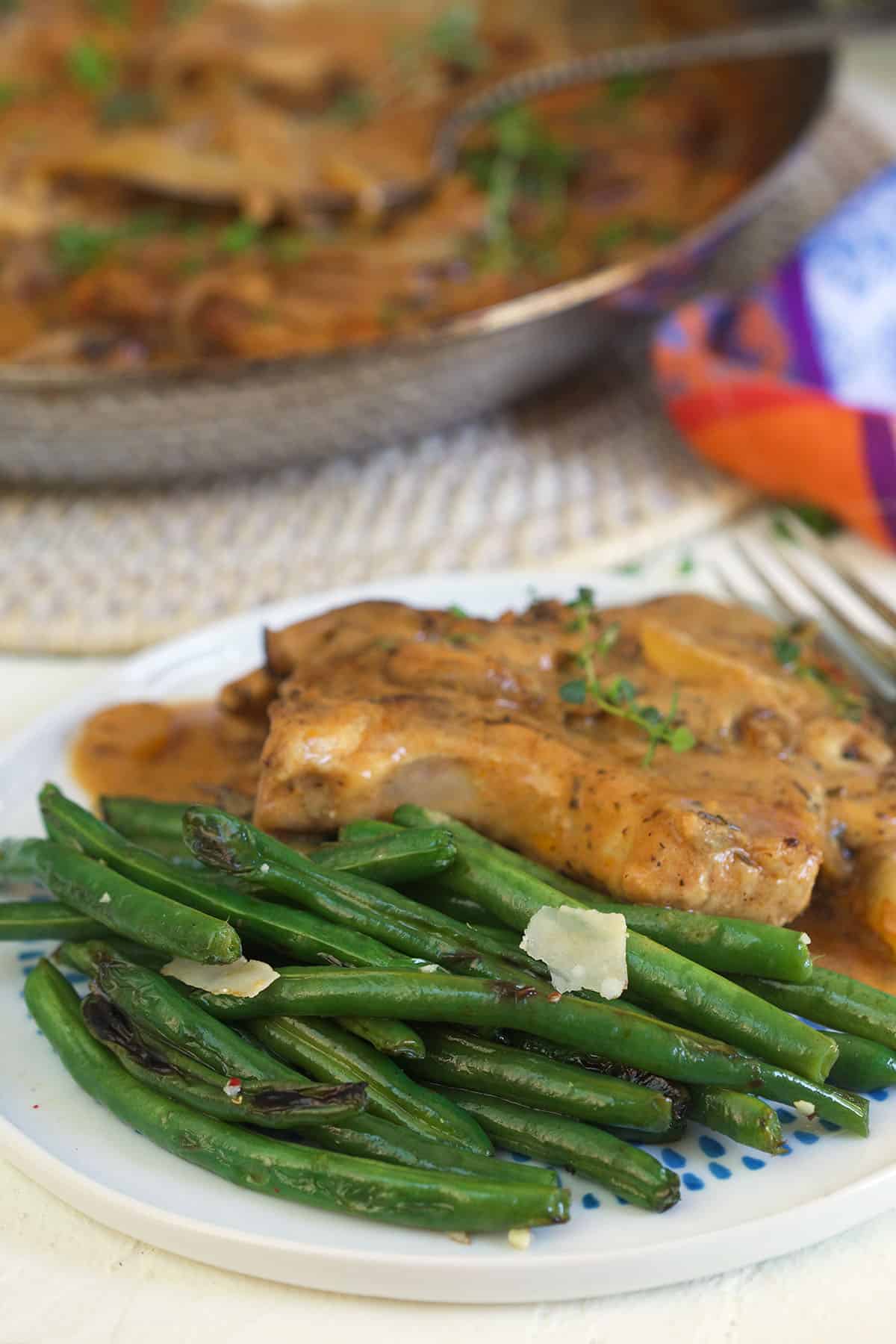 Green beans are plated with cooked chicken. 
