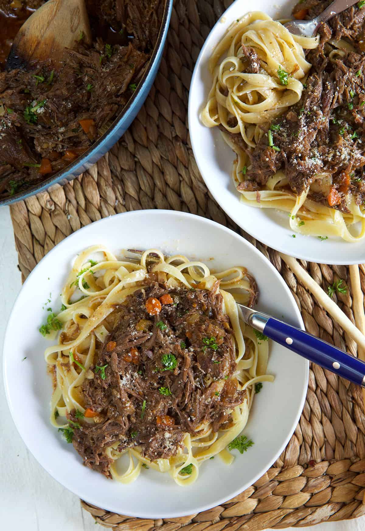 Two bowls of pasta and short rib ragu are placed on a brown place mat.