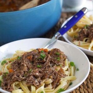 A blue fork is placed in a white bowl filled with noodles and short rib ragu.