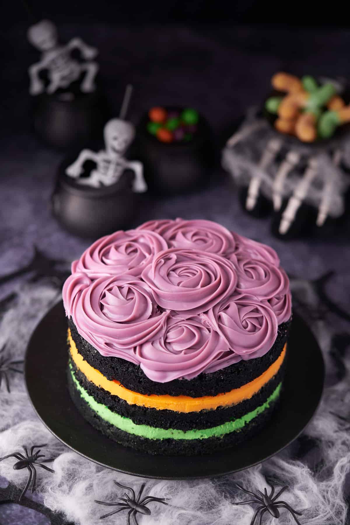 A layered cake is topped with purple icing. Skeletons are in the background. 