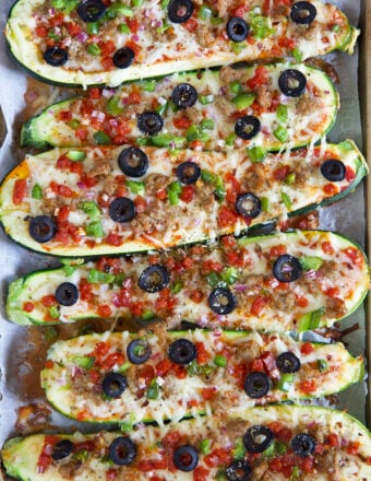 Multiple zucchini boats are placed on a baking sheet, and they're fully cooked.