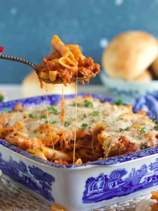 A serving of mostaccioli is being lifted from a blue and white baking dish.