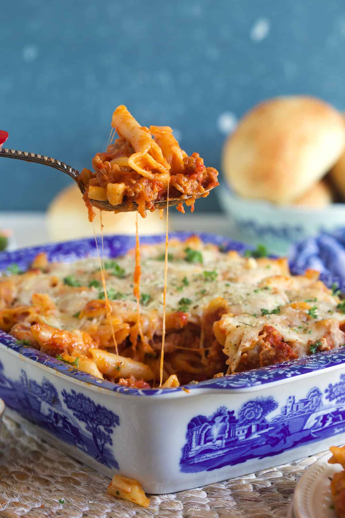 A serving of mostaccioli is being lifted from a blue and white baking dish.